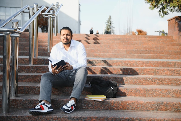 Feliz estudante indiano sentado nas escadas do campus universitário