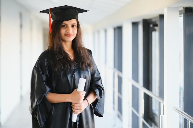 Feliz estudante universitário indiano em vestido de formatura e boné com certificado de diploma