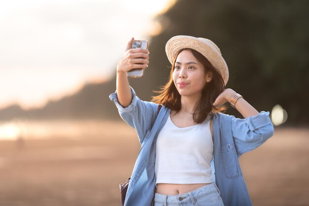 Foto feliz estudiante asiática selfie foto por teléfono inteligente durante el viaje en la hermosa playa con puesta de sol