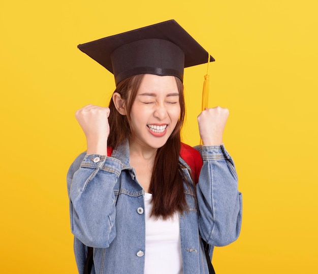 Feliz estudiante universitaria asiática con gorra de graduación con gesto de éxito