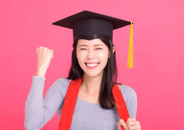 Feliz estudiante universitaria asiática con gorra de graduación con gesto de éxito