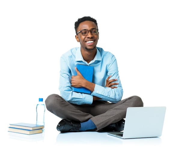 Foto un feliz estudiante universitario afroamericano sentado con una computadora portátil sobre un fondo blanco