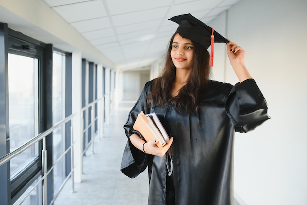 Feliz estudiante universitario indio con toga de graduación y gorra con certificado de diploma