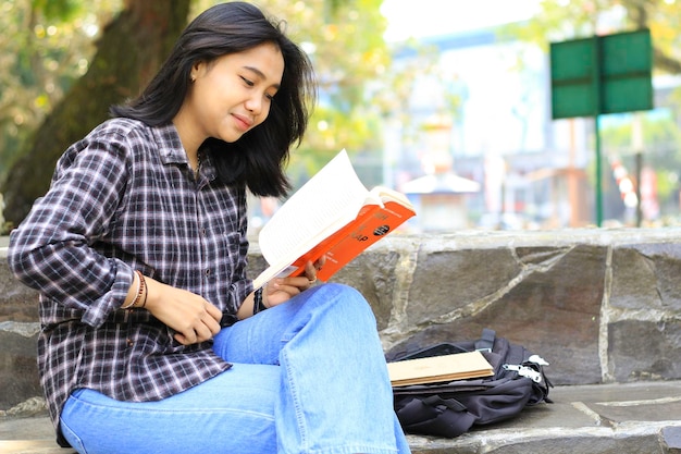 feliz y exitosa estudiante universitaria asiática disfrutando de leer un libro en el parque