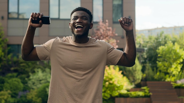 Feliz exitoso emocionado alegre tipo afroamericano con teléfono inteligente éxito ganador hombre con móvil