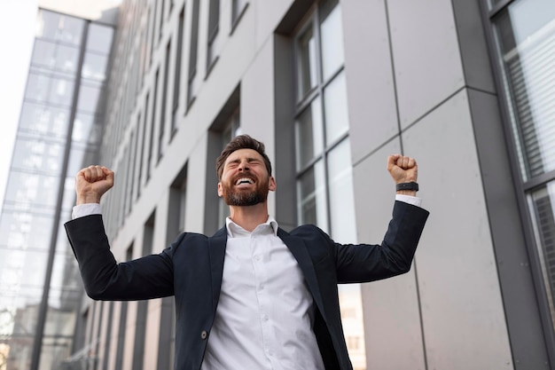 Feliz exitoso joven gerente europeo con barba en traje hace gesto de victoria