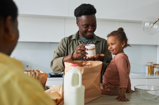 Feliz família afro-americana desempacotando produtos de sacolas juntos na cozinha