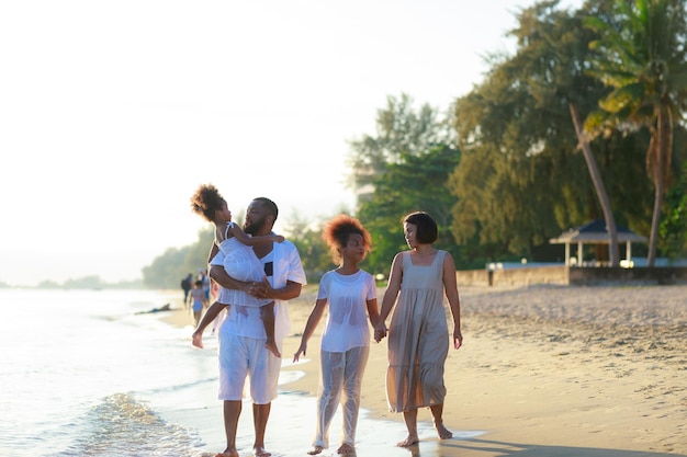 Feliz familia afroamericana tomándose de la mano y caminando juntos en la playa durante las vacaciones