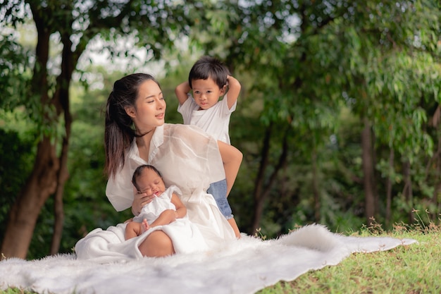 Feliz família amorosa. Asiática linda mãe e seus filhos, menina recém-nascida e um menino sentado no gramado para brincar e abraçar no parque
