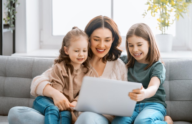 Feliz familia amorosa joven madre e hijas niñas usando laptop