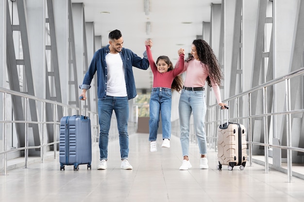 Feliz familia árabe de tres divirtiéndose juntos mientras caminan en el aeropuerto