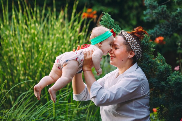 Feliz familia armoniosa al aire libre. La madre levanta al bebé, riendo y jugando en el verano.