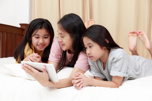 Feliz familia asiática disfrutar y relajarse en la cama en el dormitorio madre e hijas disfrutan de usar la tableta juntos