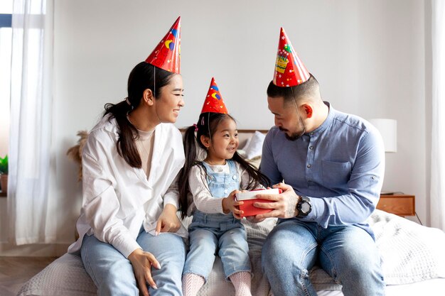 Feliz família asiática em trajes festivos comemorando o aniversário da filha e dando seu presente