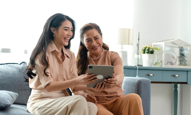 Foto feliz familia asiática hija joven y madre anciana mayor usando tableta juntos en casa