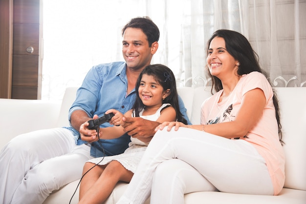 Feliz familia asiática india jugando un videojuego en casa con joystick o controlador