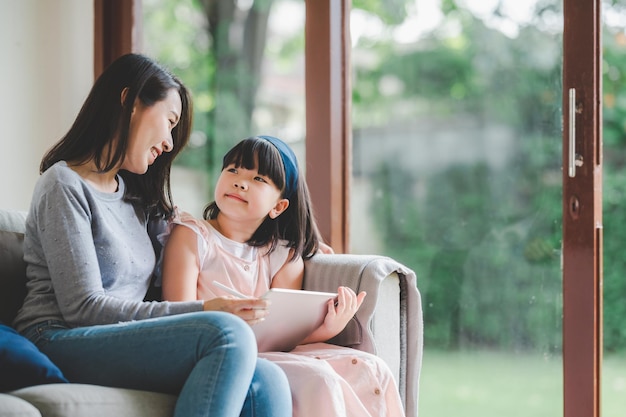 Feliz familia asiática madre e hija usando una tableta digital para estudiar juntos en casa foto enfocada en la madre