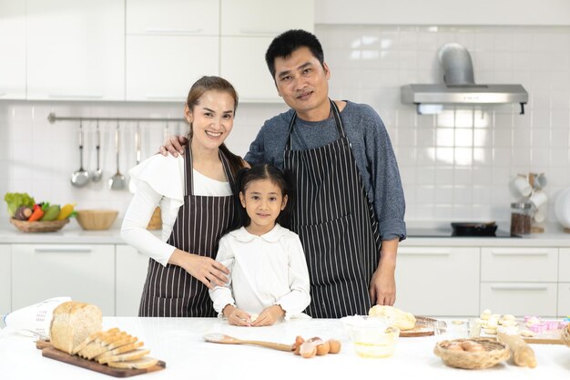 Feliz familia asiática con su hija haciendo masa preparando galletas para hornear, la hija ayuda a los padres a preparar el concepto de familia para hornear