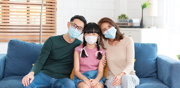 Feliz família asiática usando uma máscara para se proteger contra vírus na sala de estar de casa.