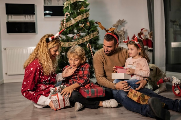 Feliz família caucasiana de quatro abrindo presentes de Natal no chão perto da árvore decorada