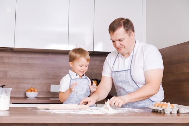 Feliz família caucasiana sorridente em aventais cozinhando e amassando massa em uma madeira