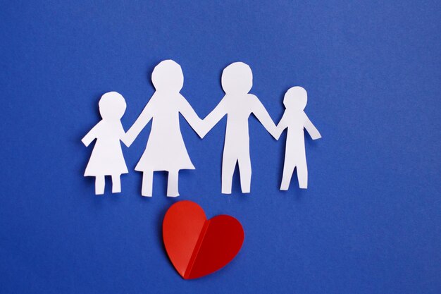 Feliz familia cortada en papel cogidos de la mano sobre fondo azul con corazón rojo