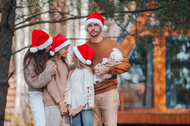 Feliz familia de cuatro en Santa hat disfrutando de las vacaciones de Navidad de fondo de su casa