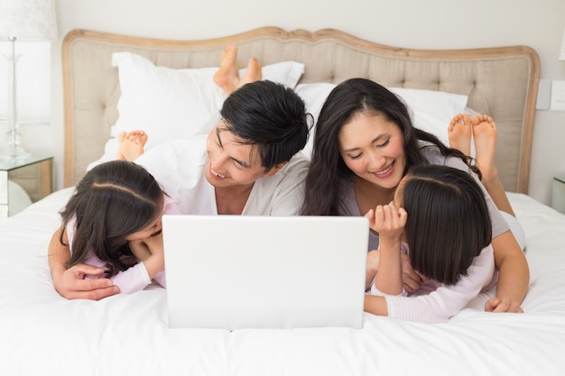 Feliz familia de cuatro usando la computadora portátil en la cama