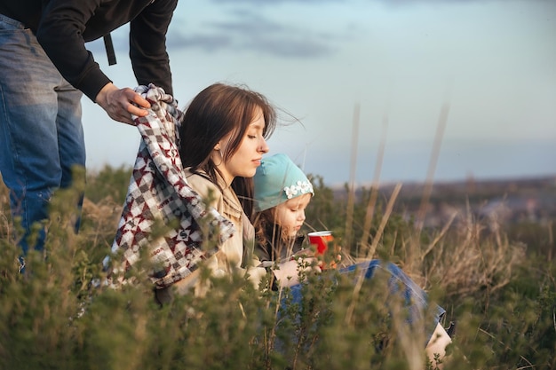 Feliz família de viajantes cobre com um cobertor e abraça sua esposa e filha na natureza