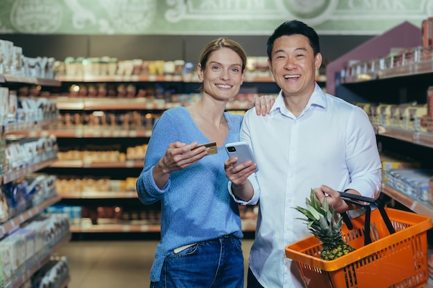 Feliz familia diversa pareja hombre y mujer compradores en el supermercado mirando a la cámara y sonriendo