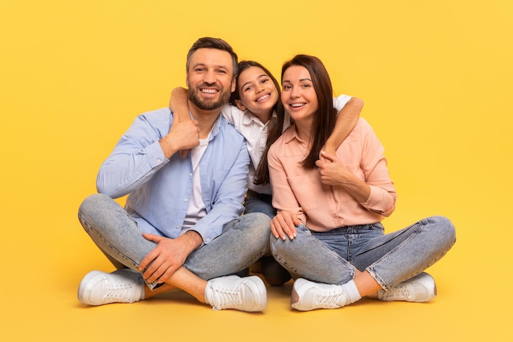 Feliz familia europea abrazándose sentados juntos contra el fondo amarillo del estudio