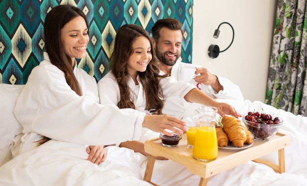 Feliz familia hermosa joven en batas de baño están tomando el desayuno por la mañana en una habitación de hotel de lujo