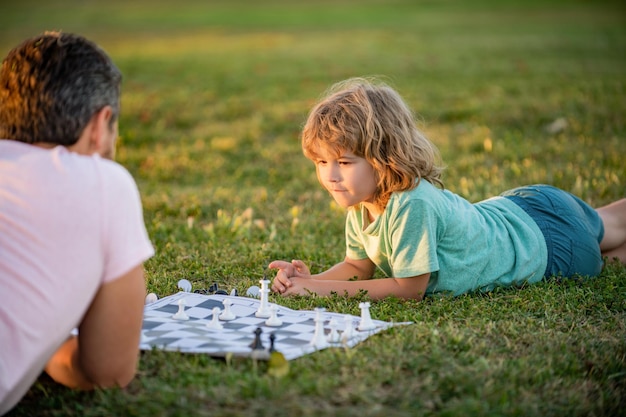 feliz familia de hombre padre e hijo jugando al ajedrez en la hierba verde en el parque al aire libre, relaciones familiares.