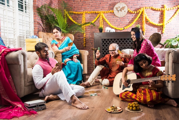 Feliz familia india jugando patti adolescente o juego de tres cartas en la noche del festival de diwali en ropa tradicional en casa