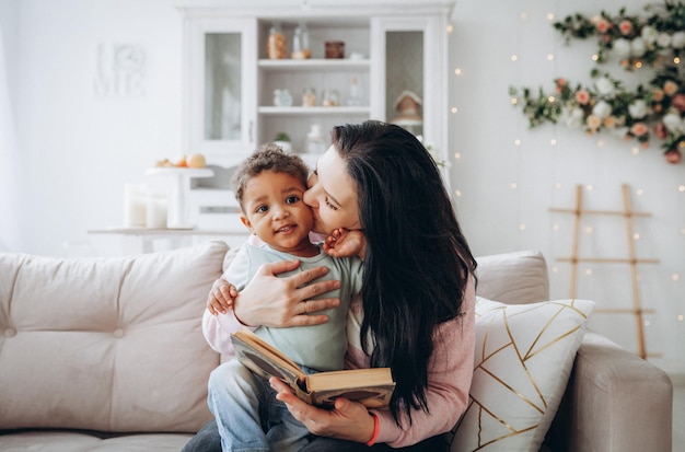 Feliz familia interracial Madre caucásica y su hijo afroamericano leyeron un libro en el sofá