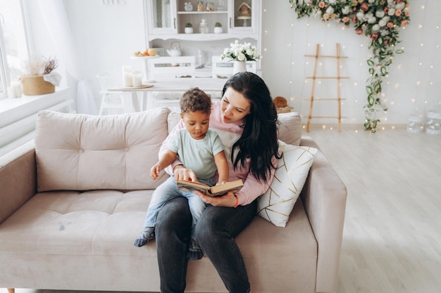 Feliz família interracial mãe caucasiana e seu filho afro-americano leram um livro no sofá