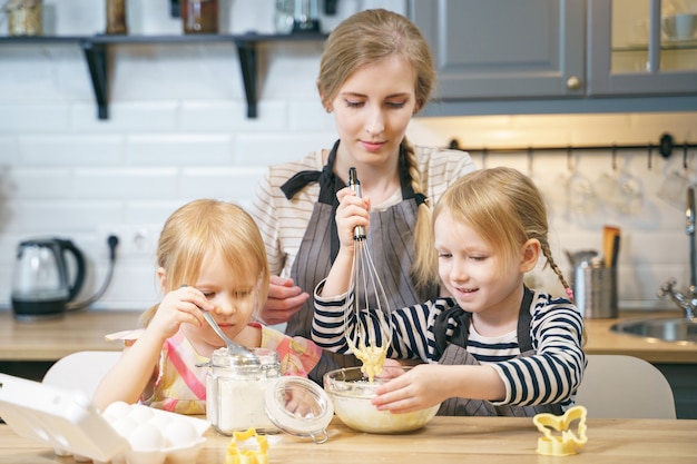 Feliz família jovem mãe e duas filhas fazendo massa