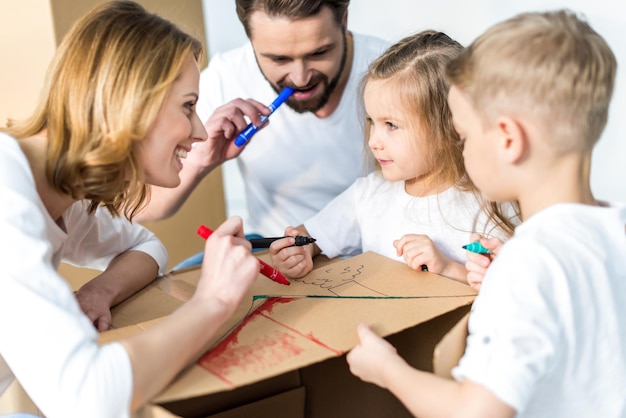 Feliz familia joven de cuatro dibujando juntos en una caja de cartón