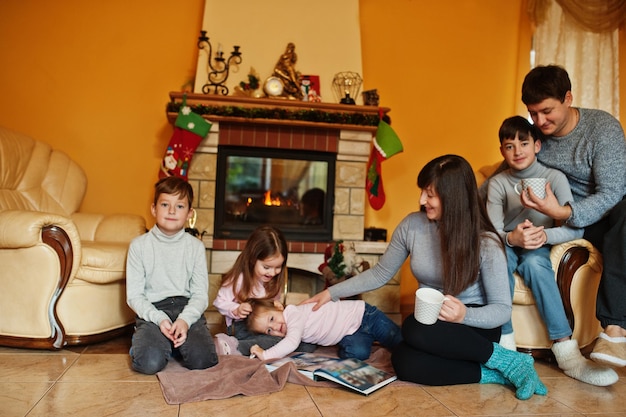Feliz familia joven y numerosa en casa junto a una chimenea en una cálida sala de estar el día de invierno