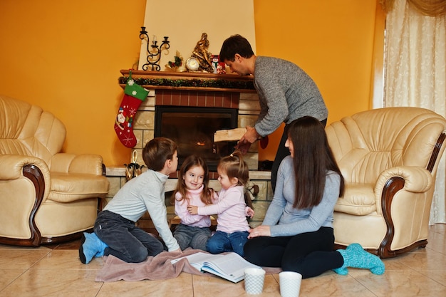 Feliz familia joven y numerosa en casa junto a una chimenea en una cálida sala de estar el día de invierno