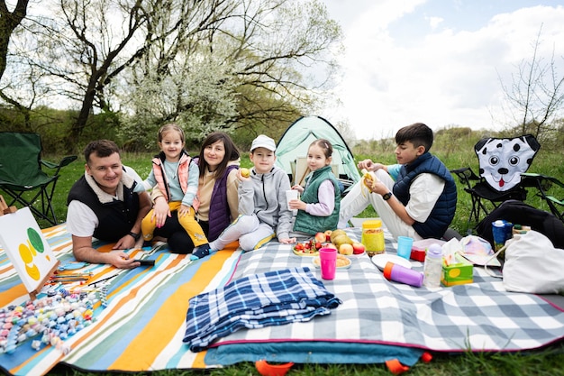 Feliz familia joven y numerosa con cuatro niños divirtiéndose y disfrutando al aire libre en una manta de picnic en el parque de primavera del jardín relajación