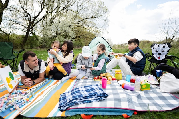 Feliz familia joven y numerosa con cuatro niños divirtiéndose y disfrutando al aire libre en una manta de picnic en el parque de primavera del jardín relajación