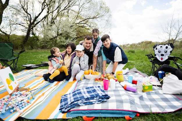 Foto feliz familia joven y numerosa con cuatro niños divirtiéndose y disfrutando al aire libre en una manta de picnic en el parque de primavera del jardín relajación