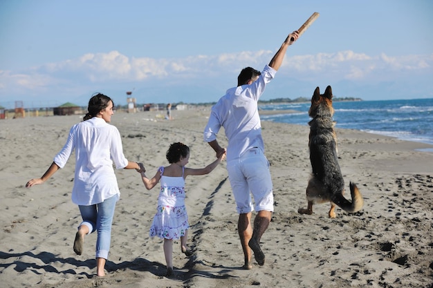 feliz familia joven vestida de blanco diviértete y juega con un hermoso perro de vacaciones en una hermosa playa