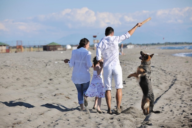 feliz familia joven vestida de blanco diviértete y juega con un hermoso perro de vacaciones en una hermosa playa