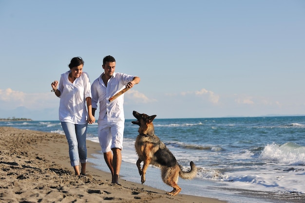 feliz familia joven vestida de blanco diviértete y juega con un hermoso perro de vacaciones en una hermosa playa