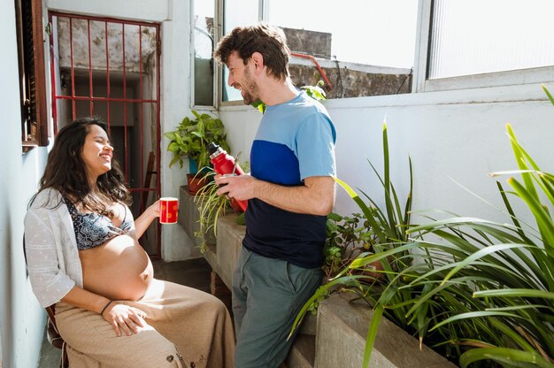 Feliz familia latina joven embarazada heterosexual en casa disfrutando bebiendo mate y charlando