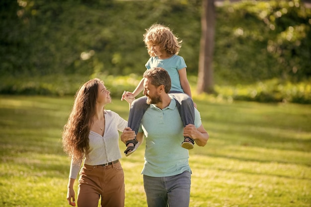 Feliz familia de madre y padre llevando a un niño sobre los hombros de crianza al aire libre de verano