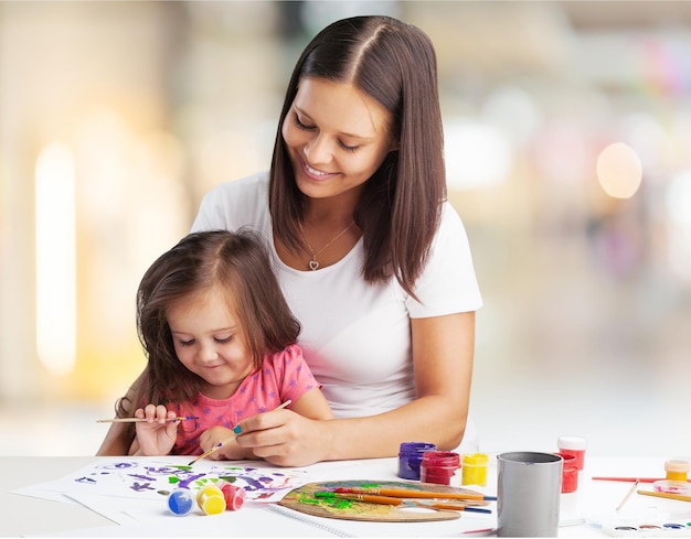 Feliz família mãe e filha juntos pintam. Mulher ajuda menina criança.