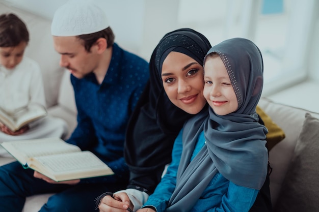 Feliz família muçulmana aproveitando o mês sagrado do Ramadã enquanto ora e lê o Alcorão juntos em uma casa moderna.